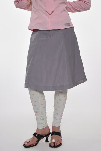 Person wearing a pink shirt, gray skirt, and patterned leggings on a white background