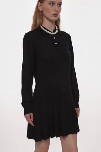 Black dress worn with a pearl necklace worn by a model on a white background
