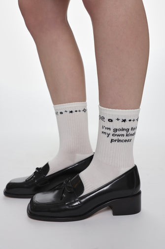 White socks with text reading "I'm going to be my own kind of princess" on the ankle with black shoes on a white background