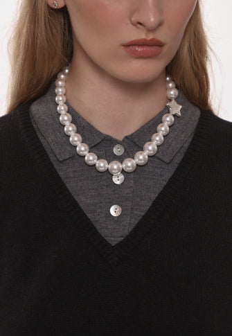 Person wearing a pearl necklace and black sweater with gray shirt underneath