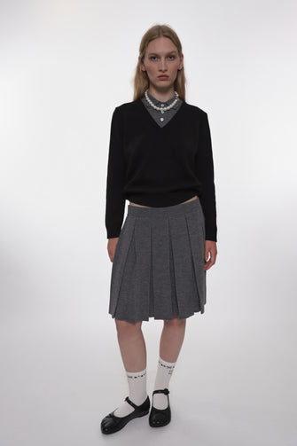 Person wearing a black sweater, gray pleated skirt, and white socks with black shoes on a white background