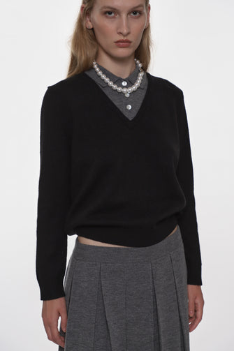 Woman wearing a black sweater with a V-neck and gray pleated pants on a white background
