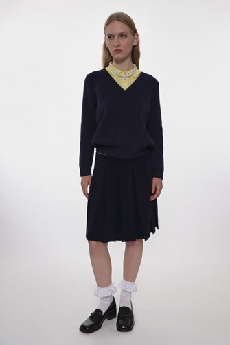 Woman wearing a navy sweater and skirt with a white blouse underneath on a white background