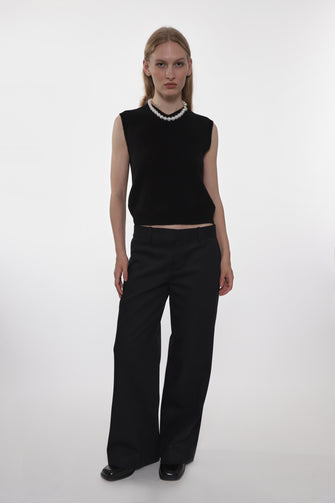 Person wearing a black sleeveless top and black wide-leg pants on a white background