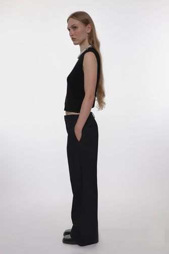 Woman wearing a black sleeveless top and wide-leg pants on a white background