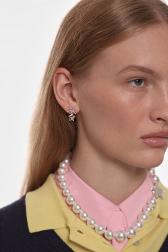 Close-up of a person wearing silver star earrings and a pearl necklace against a neutral background