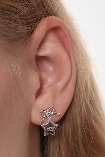 Close-up of an ear wearing a silver star-shaped earring with a bow detail.