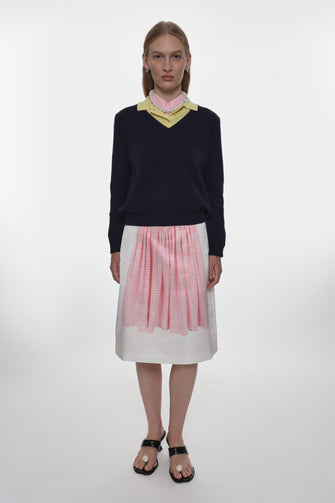 Person wearing a navy sweater with a colorful collar and a pink and white checkered skirt on a white background