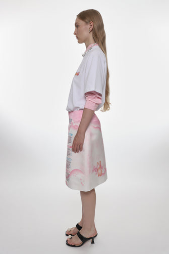 Woman wearing a white blouse with pink accents and a patterned skirt on a white background