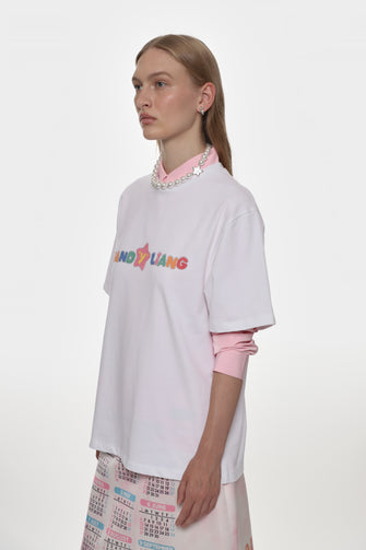 Person wearing a white oversized shirt with colorful text and pink sleeves on a white background