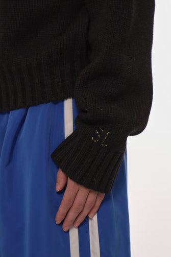 Person wearing a black sweater with a blue skirt and white stripe on a white background