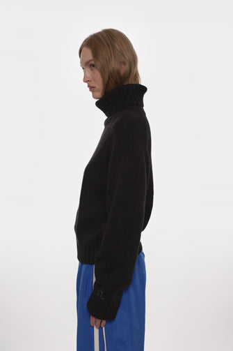 Person wearing a black turtleneck sweater and blue pants on a white background