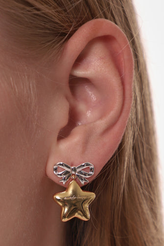 Close-up of an ear wearing a gold star-shaped earring with a silver bow detail.