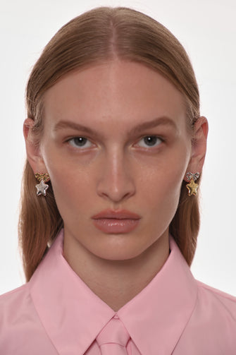 Woman wearing star-shaped earrings with a pink shirt on a white background