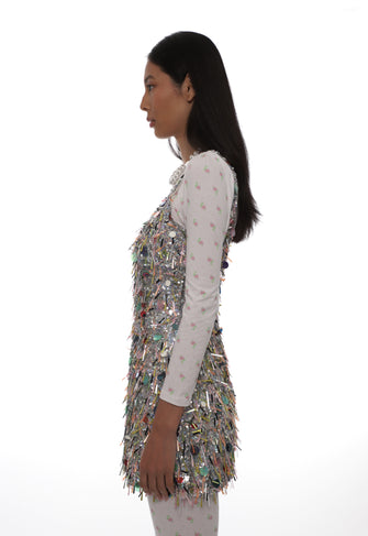 Woman wearing a multicolored sequin vest over a white long-sleeve shirt on a white background