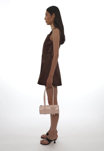 Woman in a brown dress holding a beige handbag on a white background
