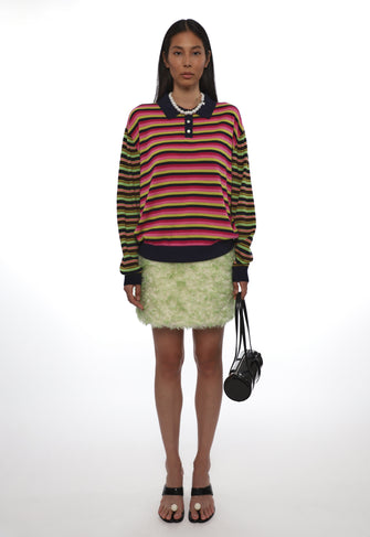 Model wearing a colorful striped sweater and green skirt with a white background
