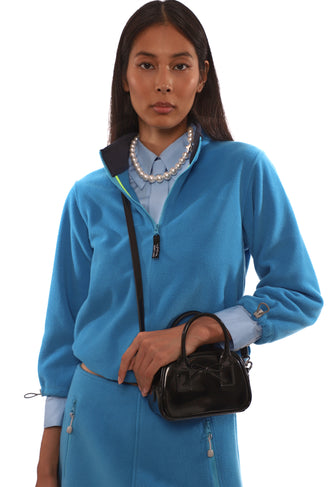 Woman wearing a blue outfit with a black crossbody handbag on a white background