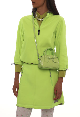 Person wearing a bright green outfit with a matching handbag on a white background