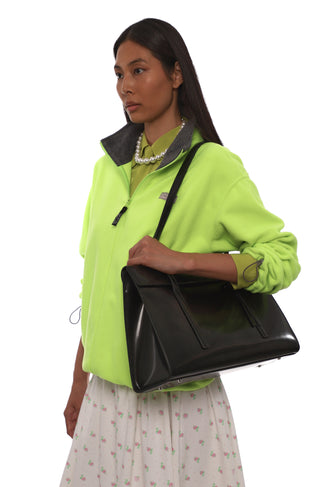 Woman holding a black bag wearing a bright green jacket on a white background