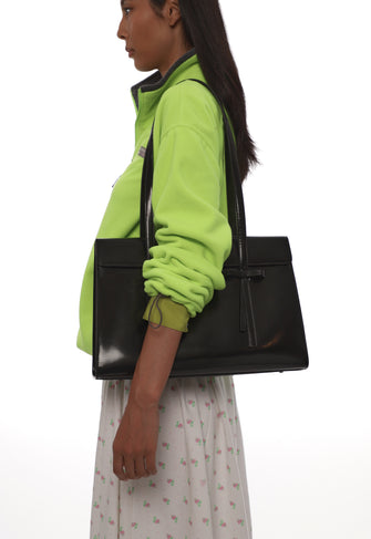 Person wearing a bright green jacket holding a black handbag on a white background
