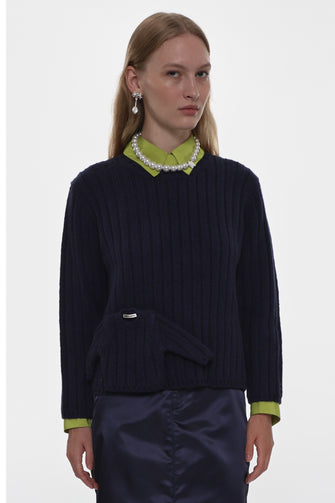 Woman wearing a dark blue sweater with a green collar and matching green cuffs and trim on a white background