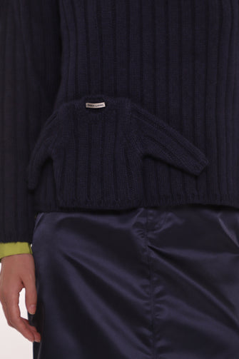 Navy blue ribbed sweater with a brand label worn by a person, with a focus on the chest area.