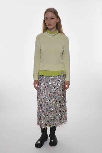 Woman wearing a light yellow sweater and patterned skirt on a white background