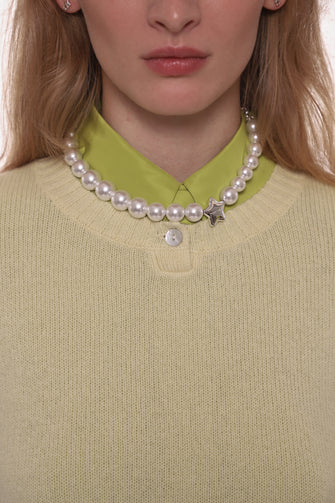 Person wearing a pearl necklace with a star charm on a light yellow sweater.