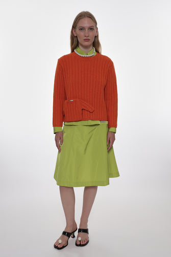 Woman wearing an orange sweater and green skirt on a white background