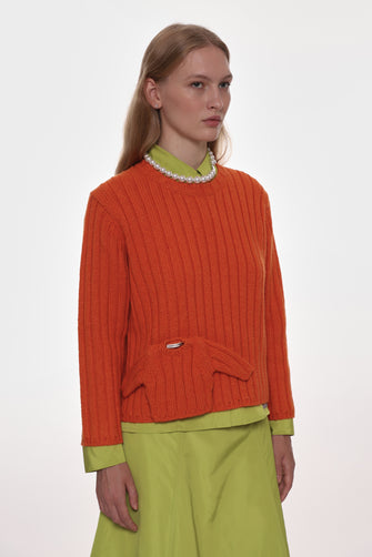 Woman wearing an orange sweater with a green collar and green pants on a white background