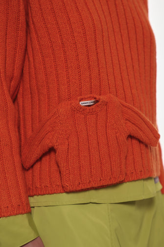 Close-up of an mini orange knitted sweater on a regular with a brand label on a white background