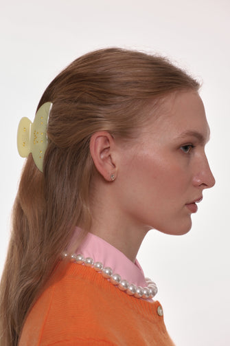 Woman wearing an orange and pink top with a yellow hair clip in her hair against a white background