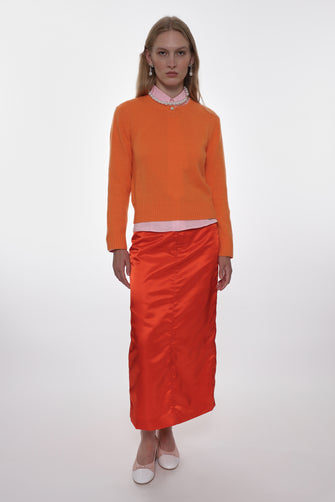 Woman wearing an orange sweater and satin skirt on a white background