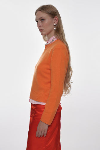 Woman wearing an orange sweater over a pink shirt with a red skirt on a white background