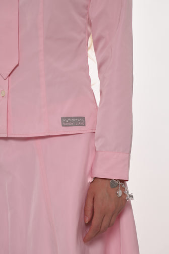 Close up of pink shirt with a visible brand label on a light pink background