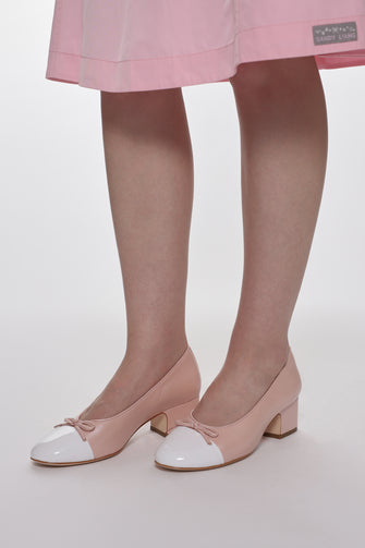 Pink shoes with white accents worn with a pink skirt on a plain background