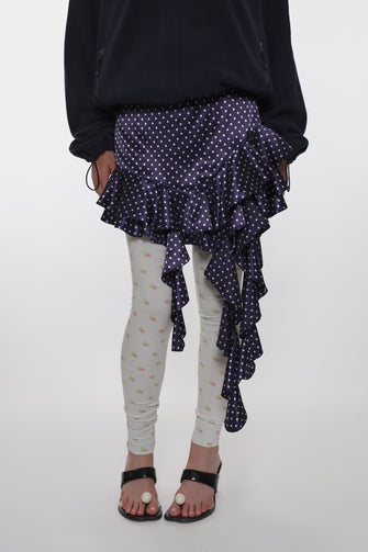Person wearing a black top with a ruffled navy skirt over white leggings on a white background