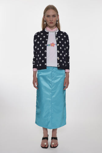 Woman wearing a polka dot swearer, white shirt with colorful design, and turquoise skirt on a white background