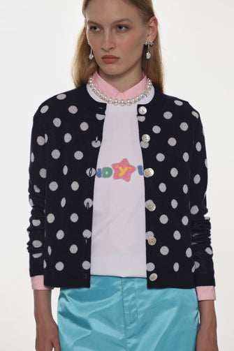 Woman wearing a polka dot cardigan over a colorful shirt with a plain background
