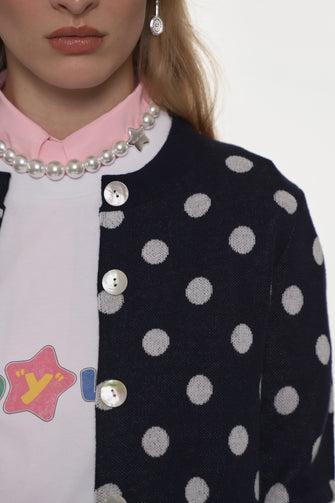Person wearing a black polka dot cardigan over a pink shirt with visible brand logo.