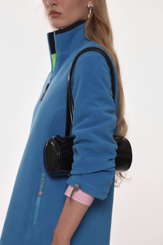 Person wearing a blue fleece dress with a black barrel shaped bag on a white background