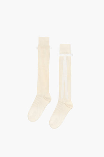 A pair of knee-high socks in ecru color with a ribbon bow on the side, made from cotton blend fabric against a white background.