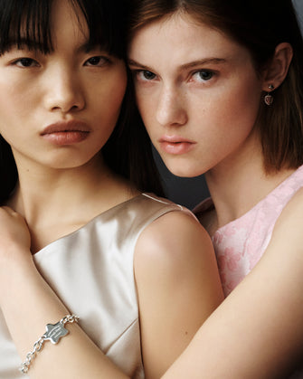 Two women pose with an arm wrapped around each other featuring a silver bracelet on the wrist