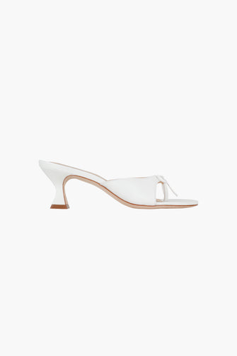 A side view of a single optic white nappa leather thong mule with a padded leather footbed and a 60mm heel against a white background