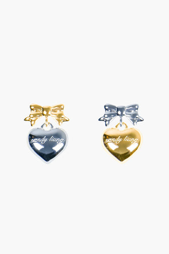 A pair of earrings with mixed metals of a bow with heart drop against a white background