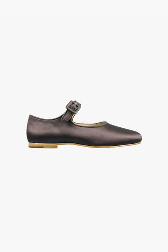 A single flat shoe with an adjustable pin-buckle strap, padded leather footbed, and a leather sole with a stacked heel, in a dark brown satin finish against a white background