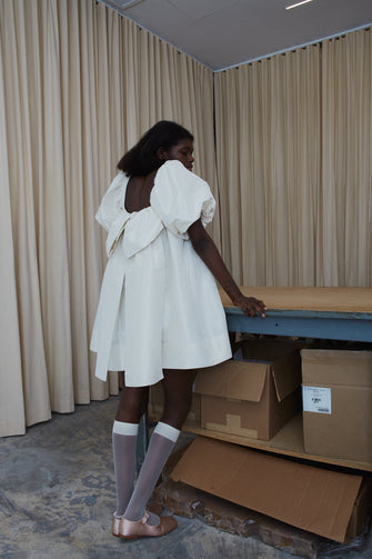 Woman wearing a short babydoll wedding dress with puff sleeves against a work table