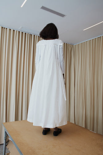 A model wearing a white bridal dress with long sleeves and a square neckline standing on a wooden table