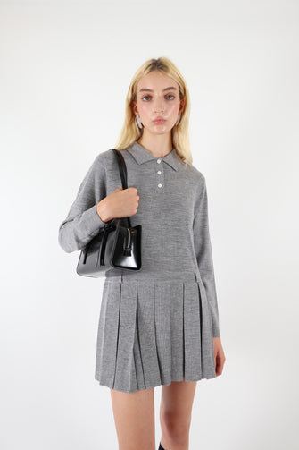 A woman wears black rectangular handbag with a bow detail on the side with a grey dress against a white background